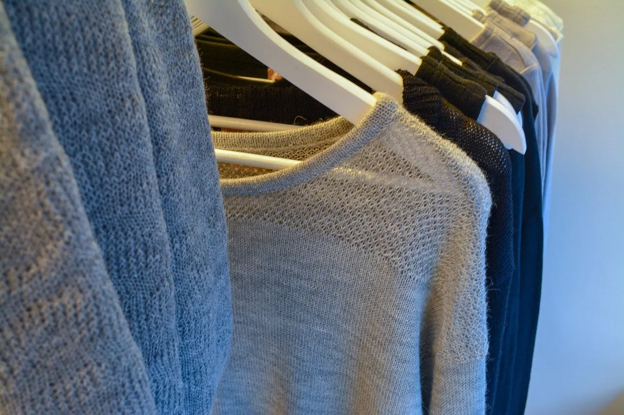 Graue und blaue Strickpullover auf weißen Bügeln an einer Kleiderstange.