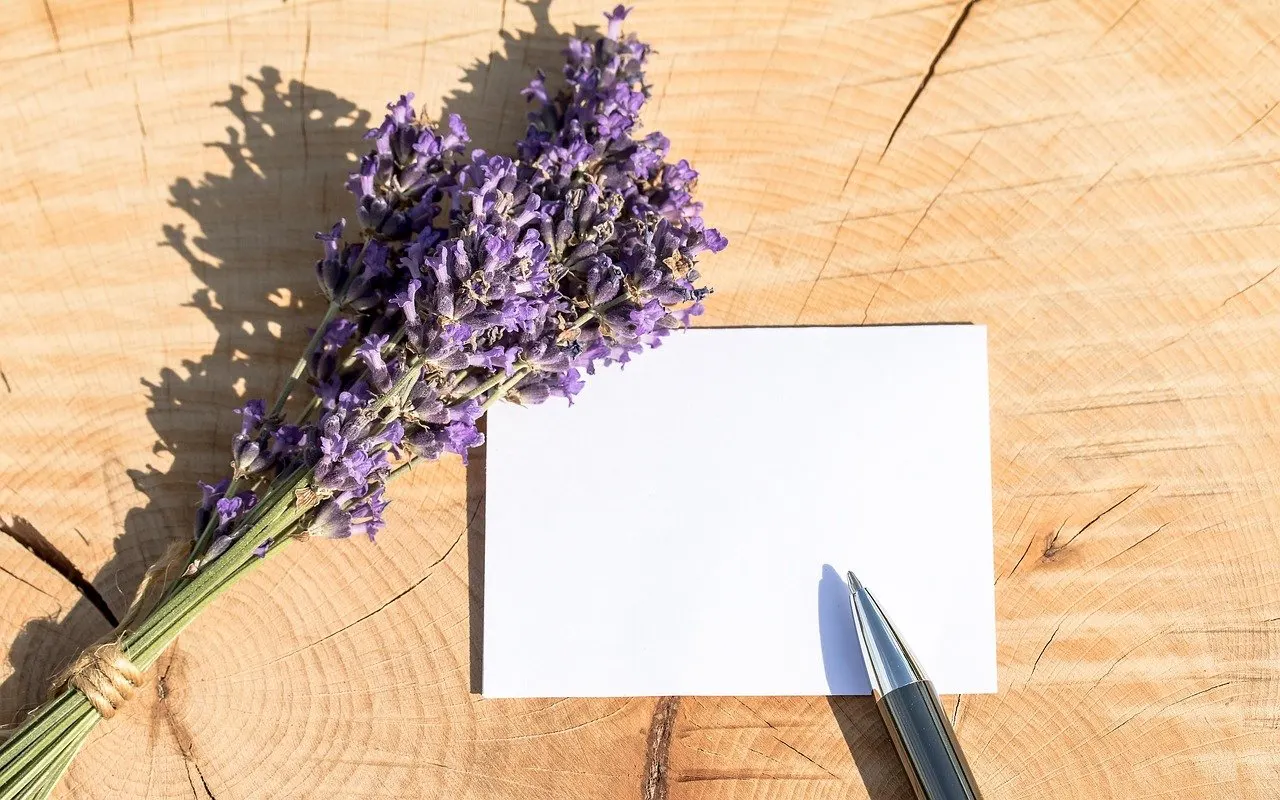 Leere weiße Karte mit silbernem Stift und lila Lavendelbund auf hellem Holzuntergrund mit Jahresringen.