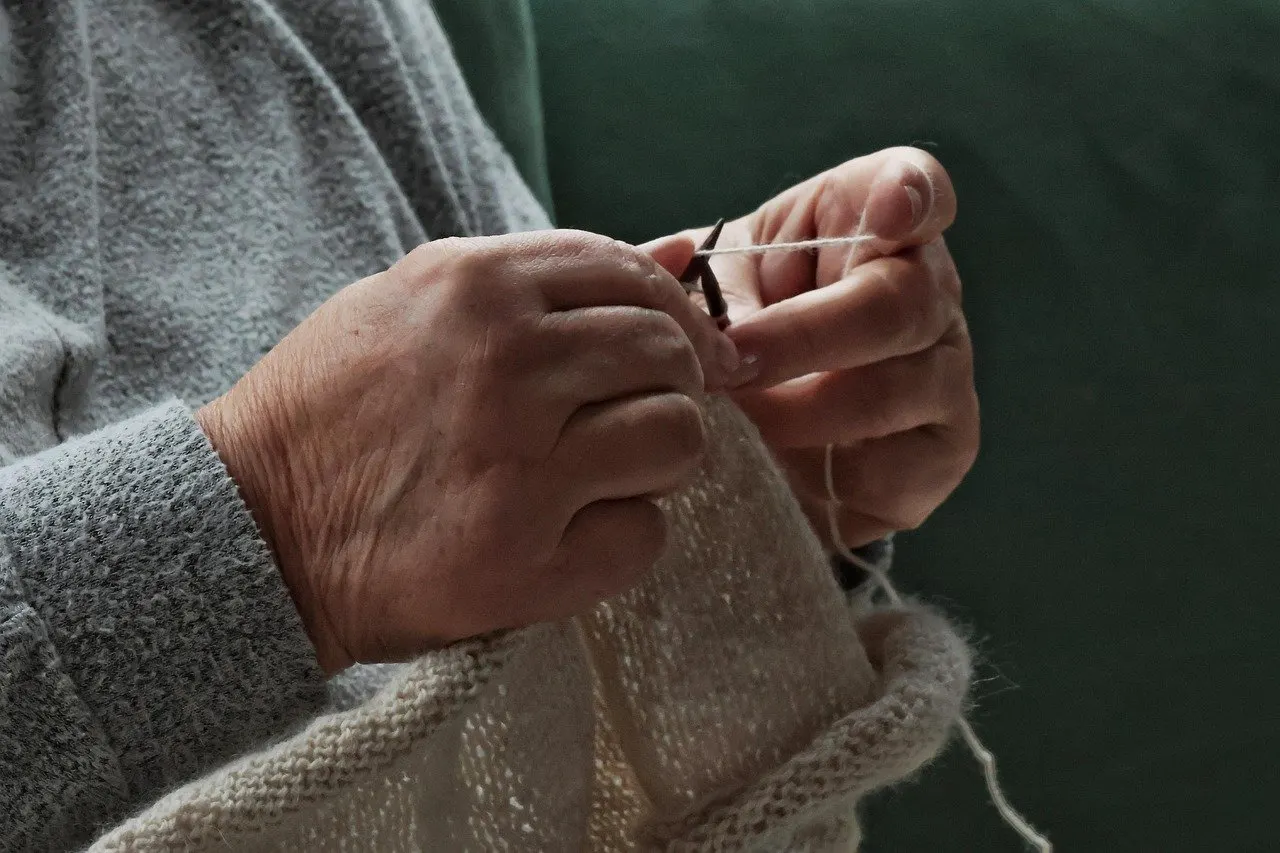 Nahaufnahme zweier Hände, die mit Stricknadeln und hellem Garn an einem Strickstück arbeiten.