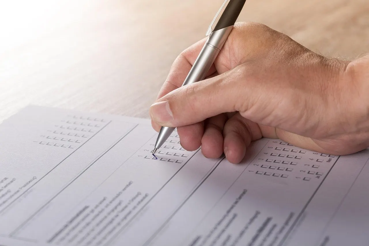 Hand mit Stift kreuzt Kästchen auf einem Formular mit Ankreuzfeldern an.